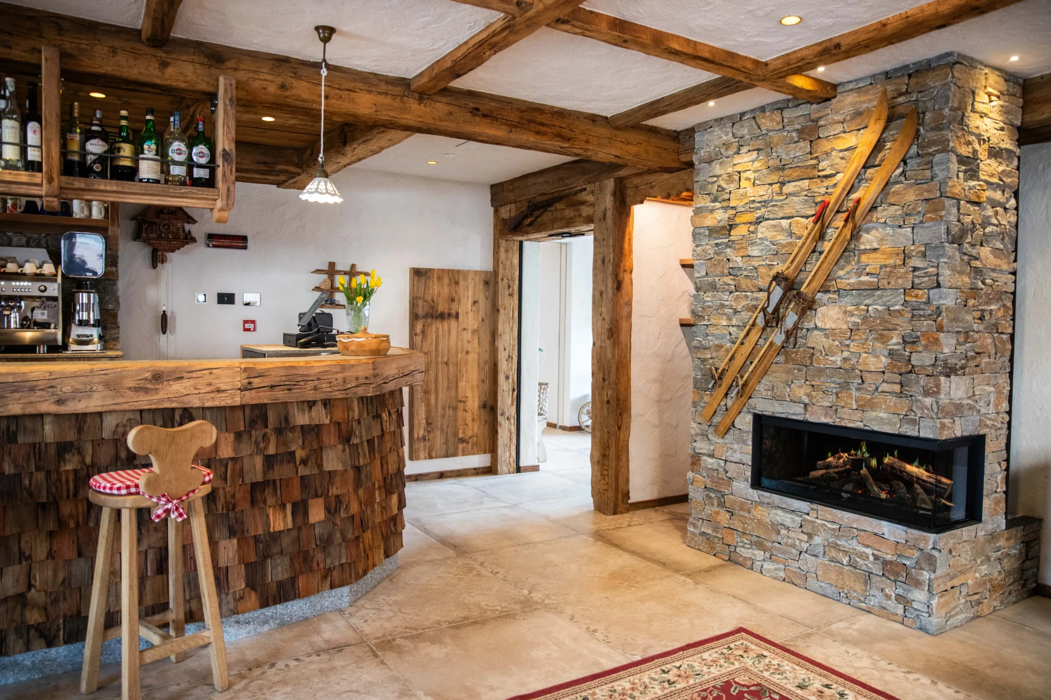 Interno accogliente di un bar rustico con camino in pietra e sci appesi.