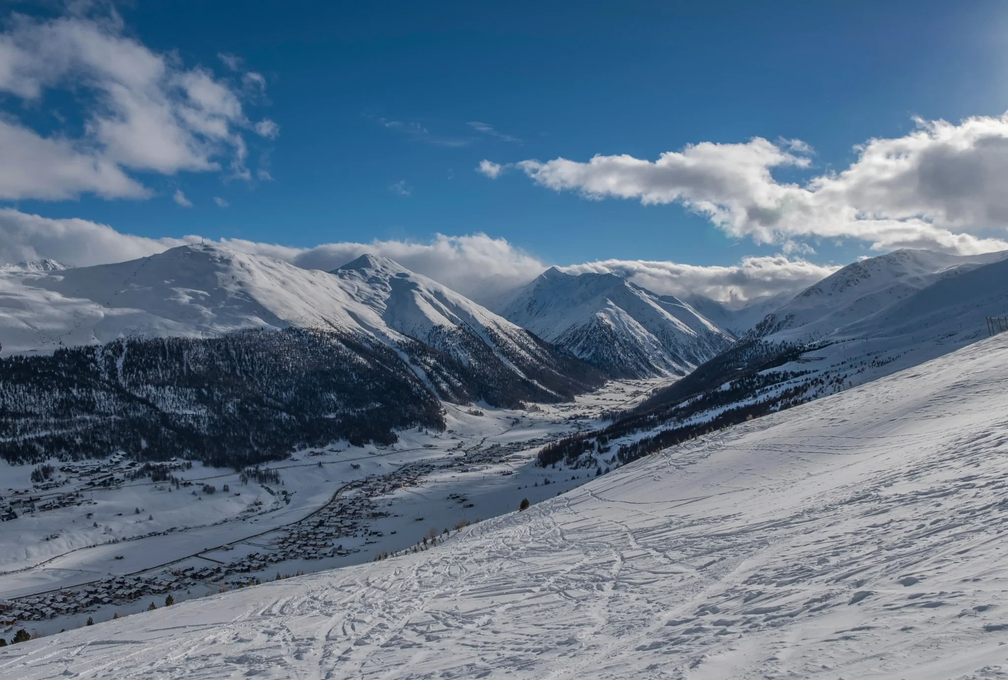 Panorama di montagne innevate sotto un cielo azzurro con nuvole soffici.