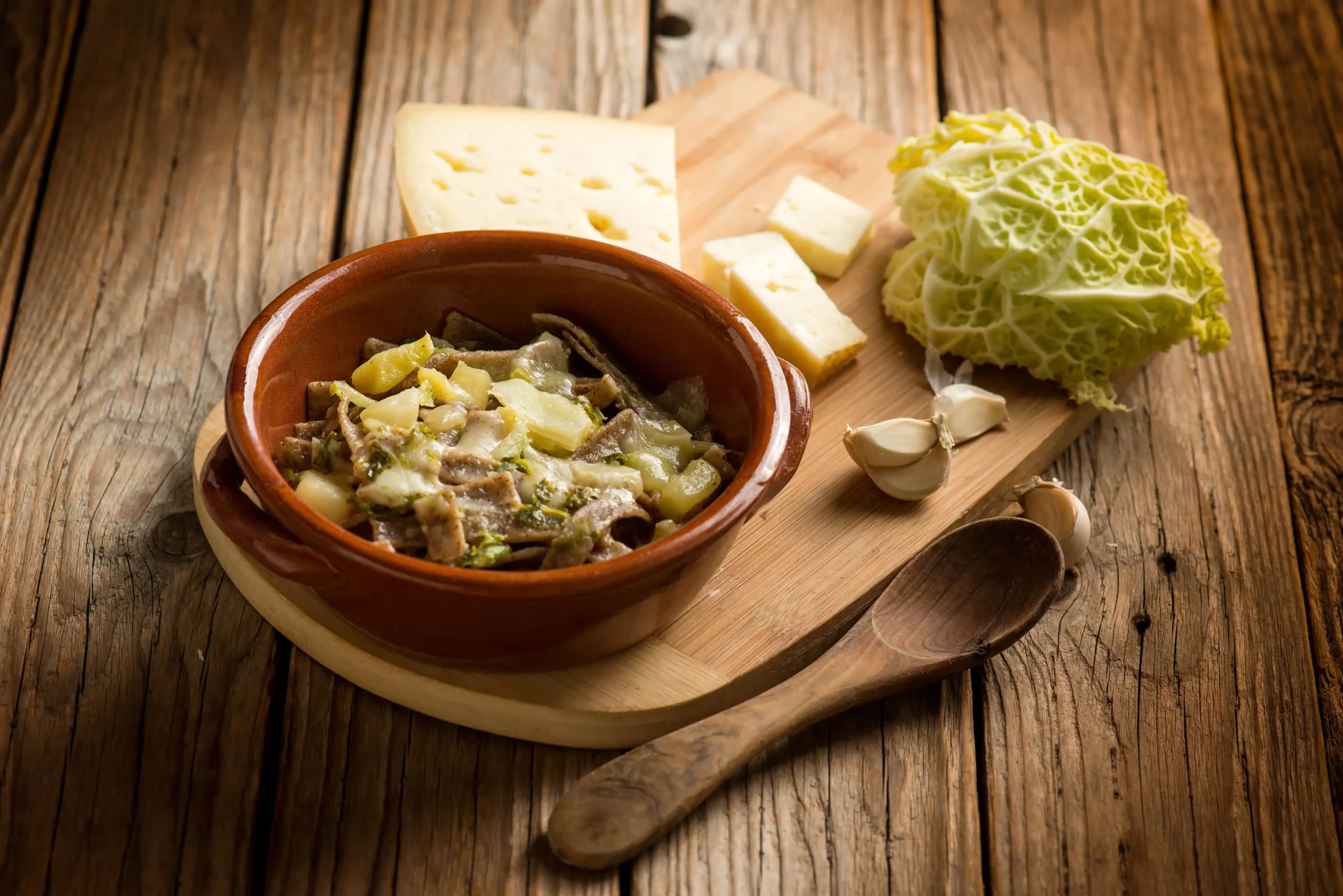 Piatto di pizzoccheri con formaggio, patate e verza su tavola rustica.