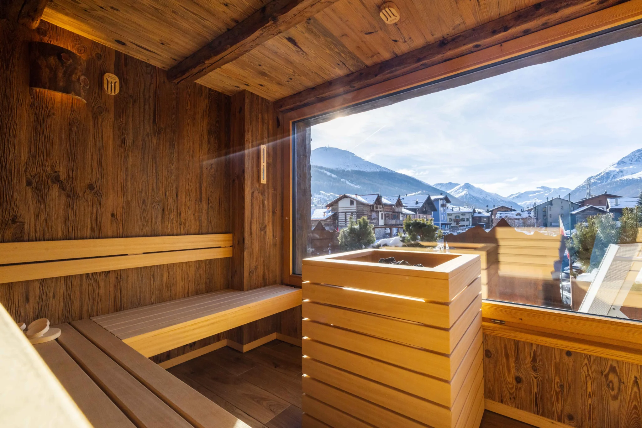 Sauna in legno con finestra panoramica su un paesaggio montano innevato.