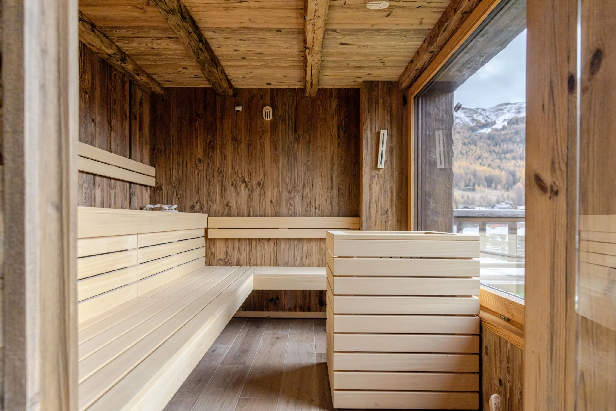 Interno di una sauna in legno con vista panoramica sulle montagne innevate.