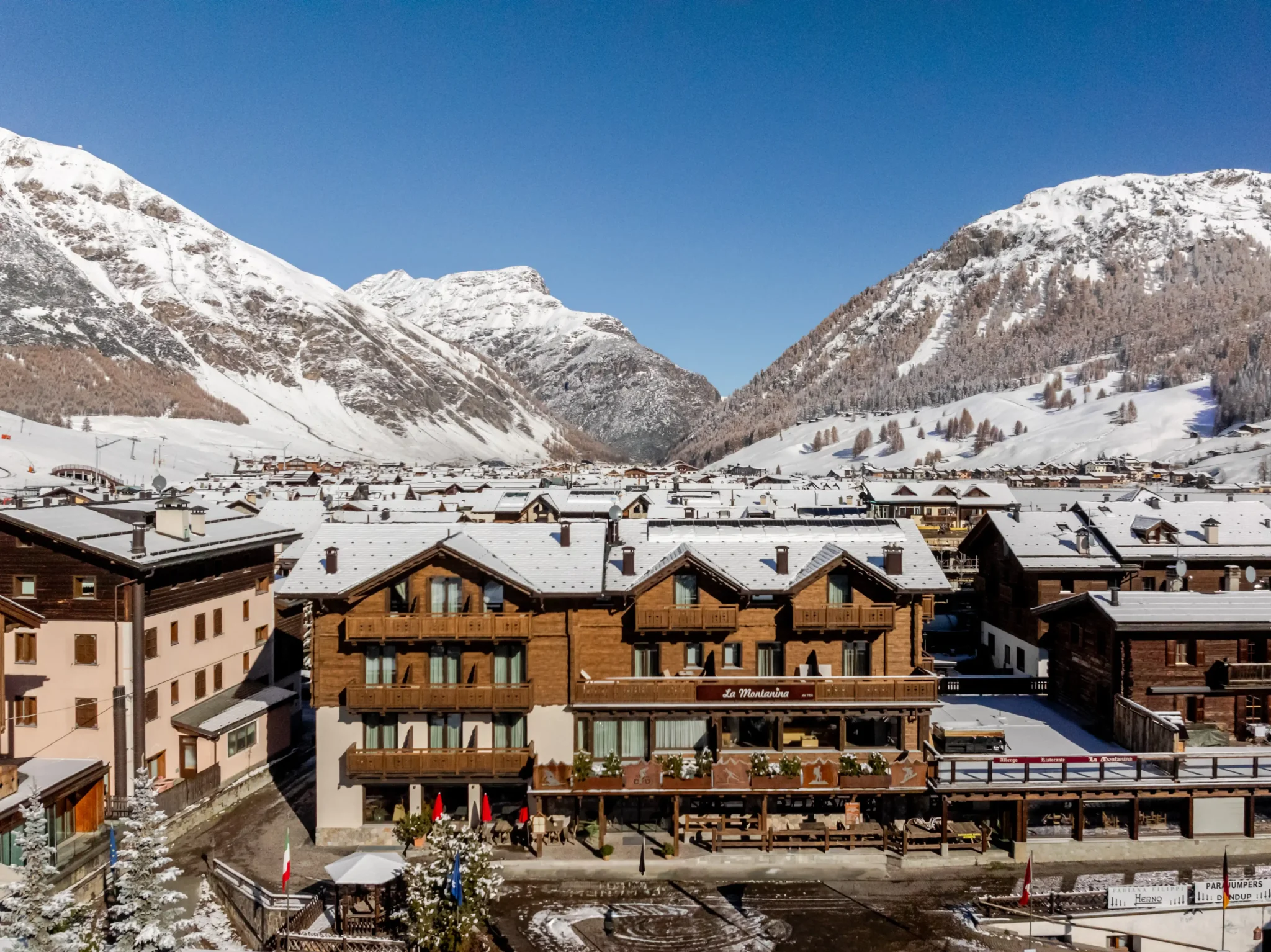 Vista di un paesino di montagna innevato con chalet in legno e montagne sullo sfondo.