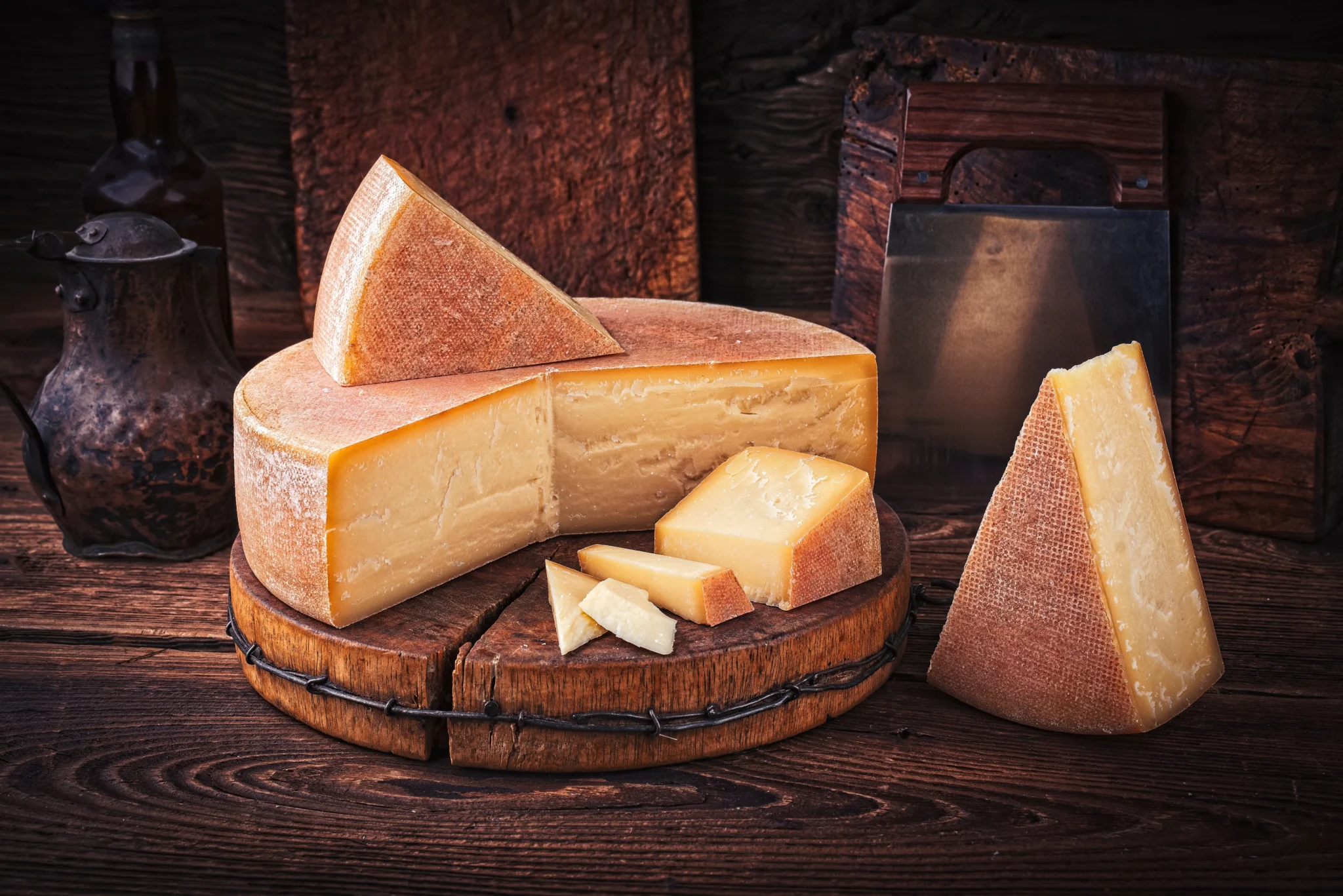 Formaggio stagionato su tagliere di legno con coltello antico sullo sfondo.