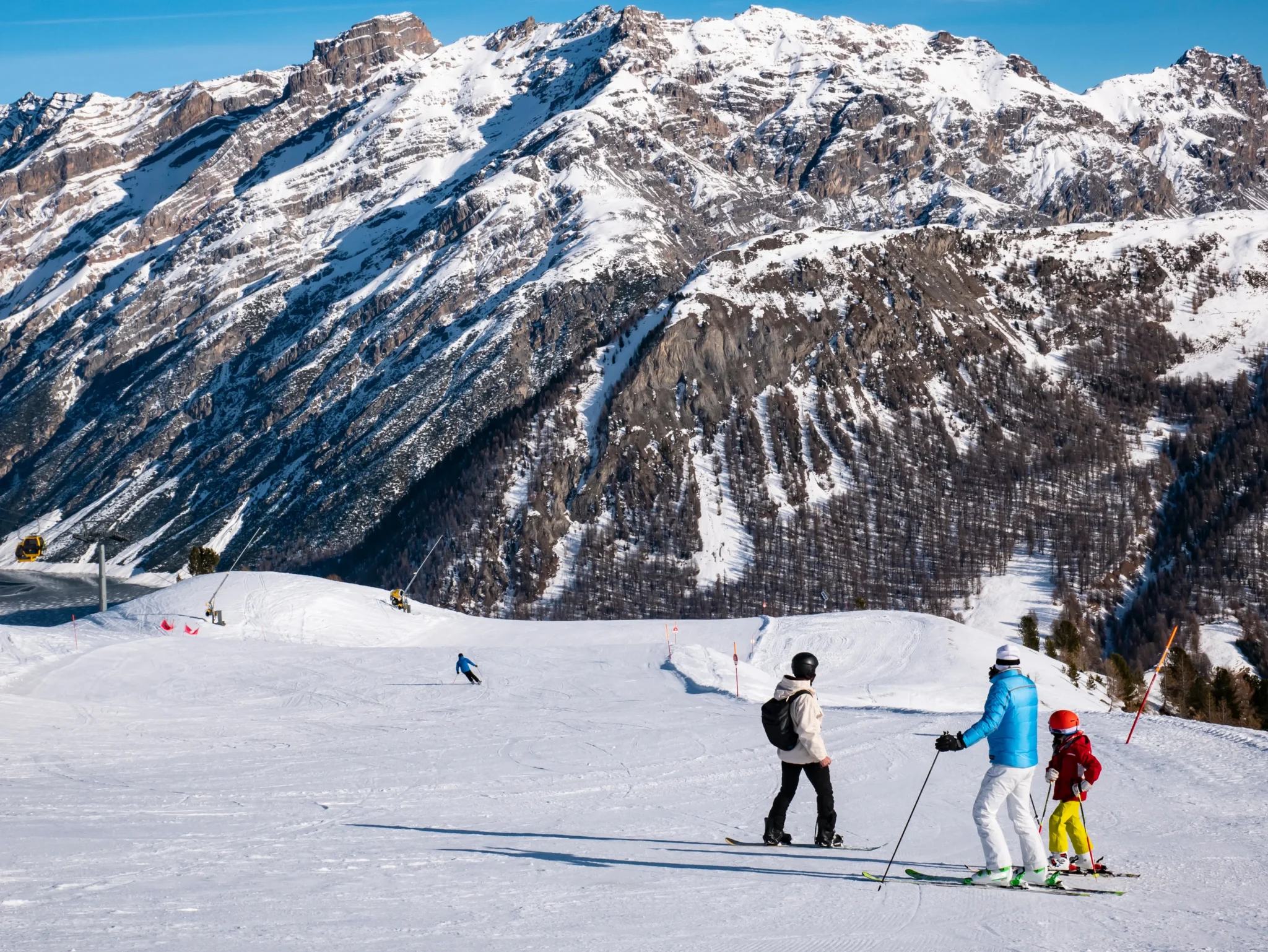 Sciatori su una pista innevata con montagne maestose sullo sfondo.