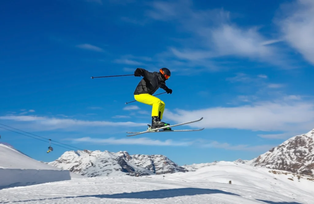 Sciatore in salto su una pista innevata con cielo blu.