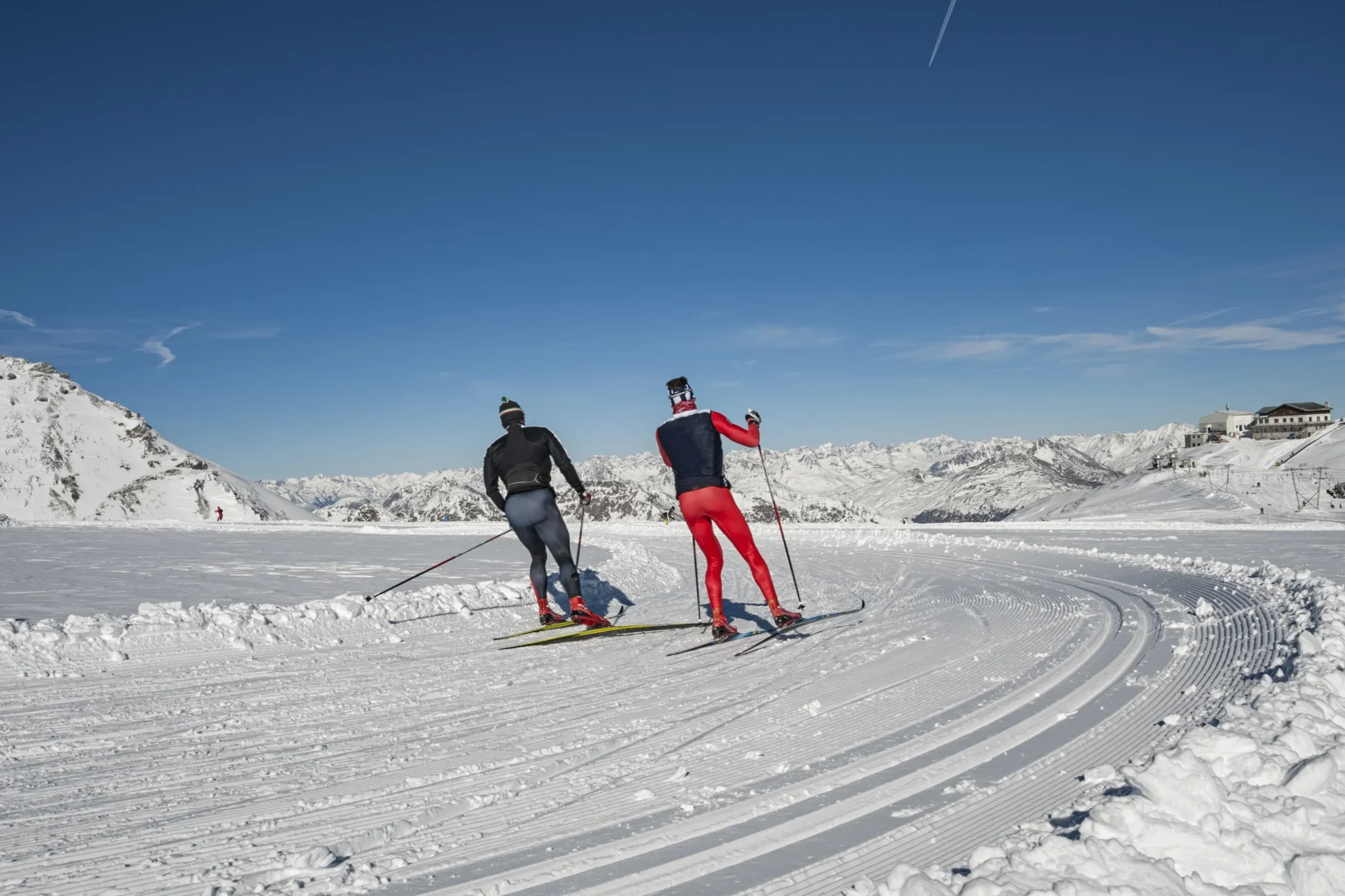 Due sciatori di fondo su una pista innevata circondata da montagne.