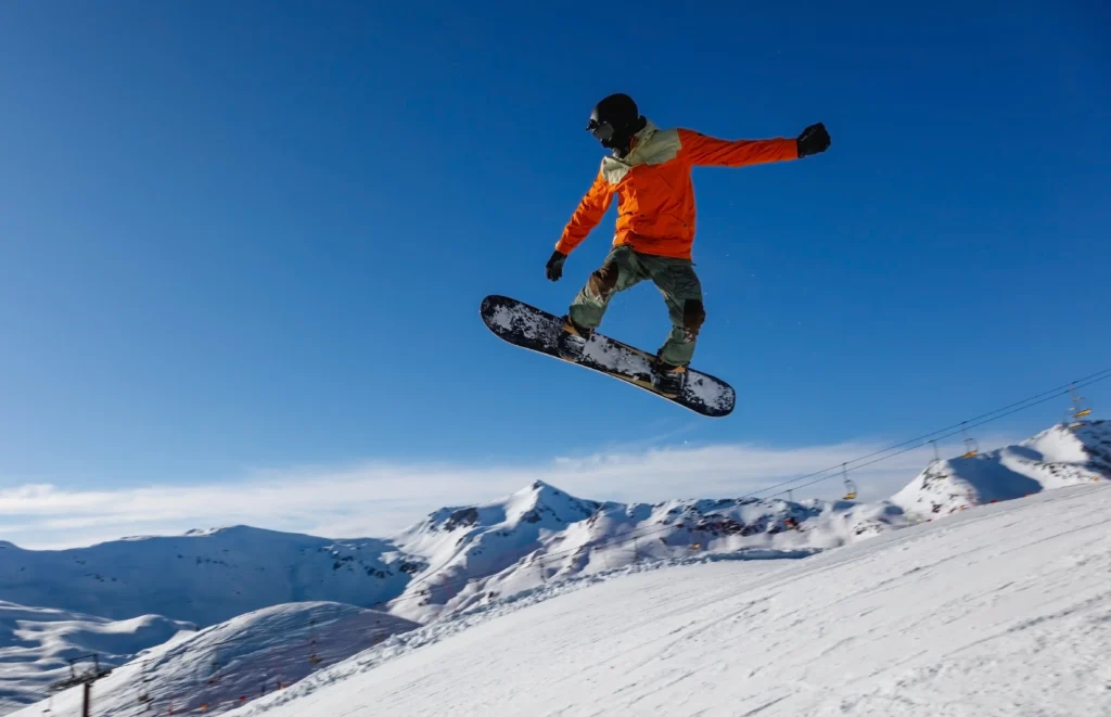 Snowboarder esegue un salto su una pista innevata con lo sfondo di montagne.