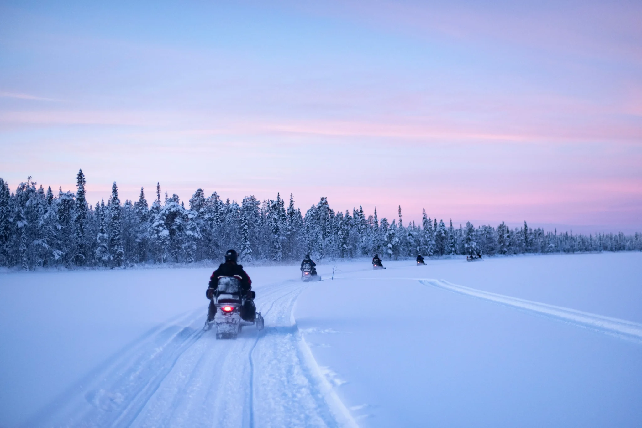 Motoslitte che attraversano un paesaggio innevato al tramonto.
