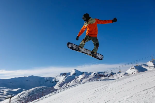 Snowboarder esegue un salto su una pista innevata con lo sfondo di montagne.